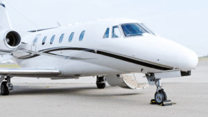 White private jet with open door and stairway, parked on airport tarmac under clear skies.