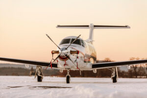 Single-engine turboprop airplane parked on a snowy runway at sunrise, prepared for winter flight operations.