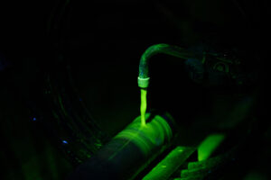 Fluorescent green liquid applied to a metal cylinder under UV light during aircraft non-destructive testing.